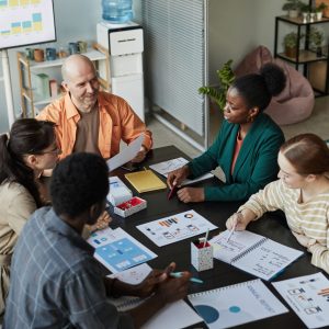 High angle view of creative business team at meeting table discussing project with smiling bald man listening to colleagues